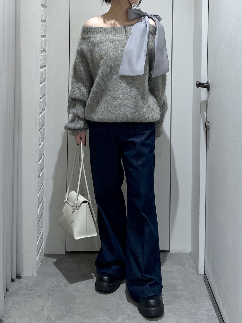 グレー系のニット/セーター、ブルー系のデニムパンツ、ホワイト系のショルダーバッグを着用したレディースの冬コーディネートの2枚目の写真