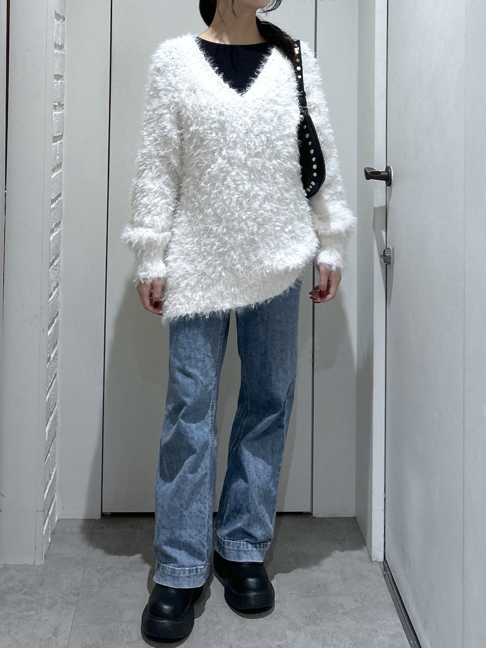 ホワイト系のニット/セーター、ブラック系のショルダーバッグ、ブルー系のデニムパンツを着用したレディースの冬コーディネートの3枚目の写真