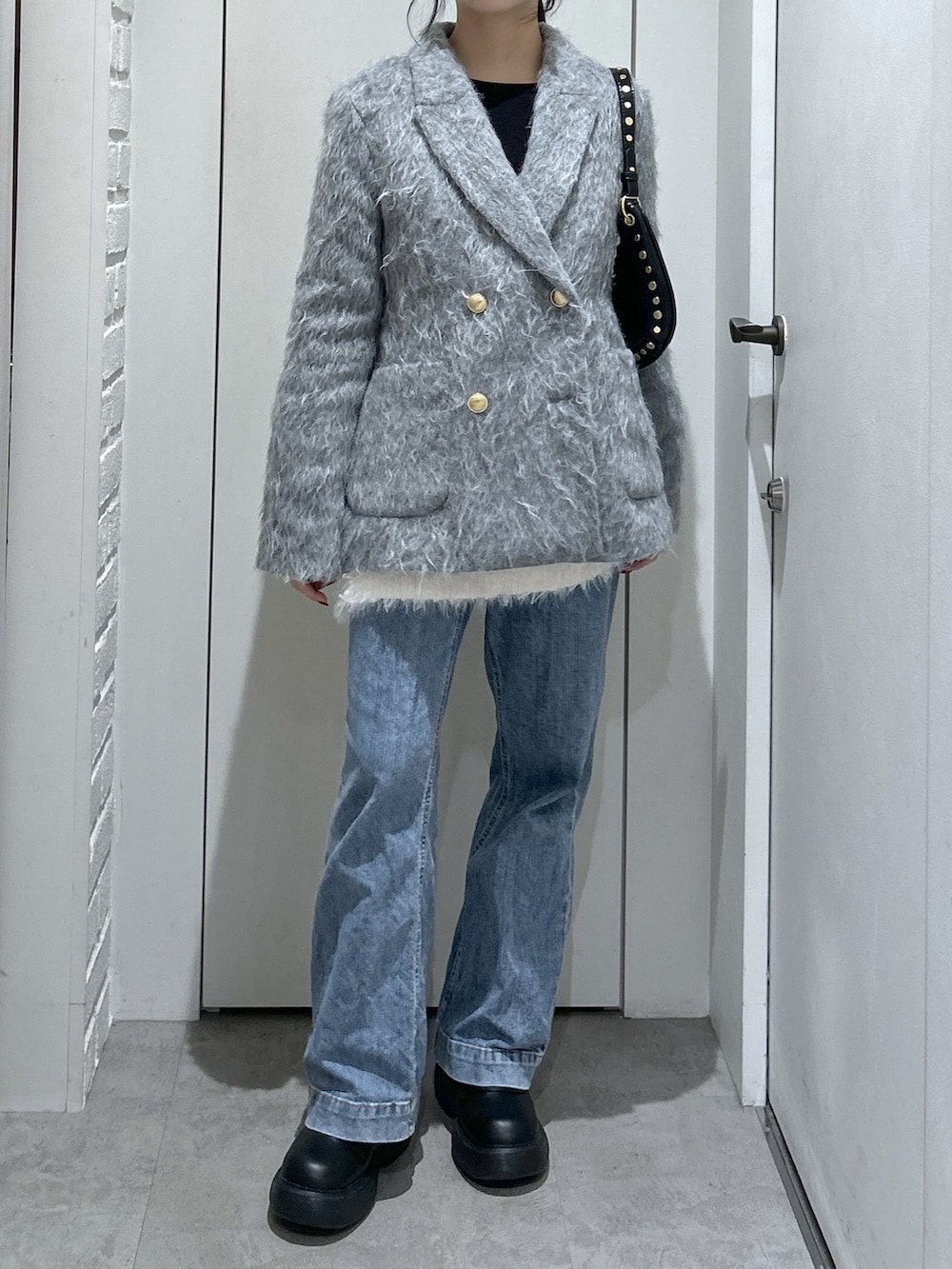 ブルー系のデニムパンツ、ホワイト系のニット/セーター、ブラック系のショルダーバッグを着用したレディースの冬コーディネートの2枚目の写真