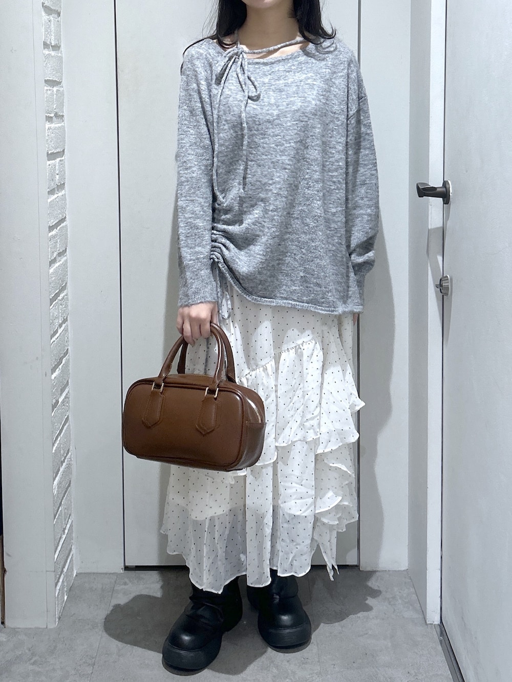 グレー系のニット/セーター、ブラウン系のハンドバッグ、ホワイト系のスカートを着用したレディースの春コーディネートの2枚目の写真