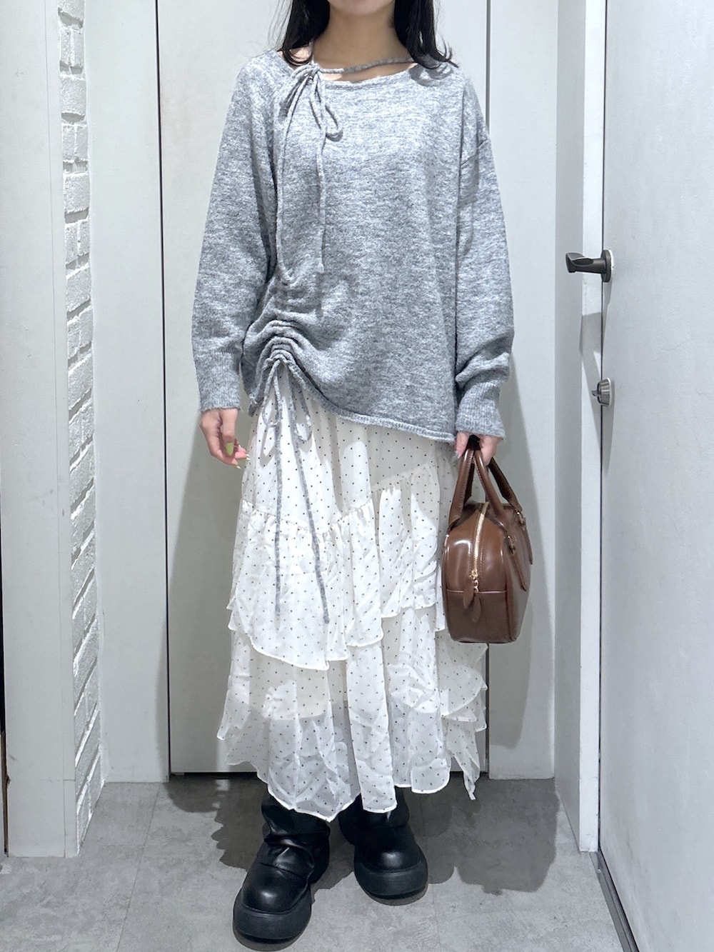 グレー系のニット/セーター、ブラウン系のハンドバッグ、ホワイト系のスカートを着用したレディースの春コーディネートの3枚目の写真