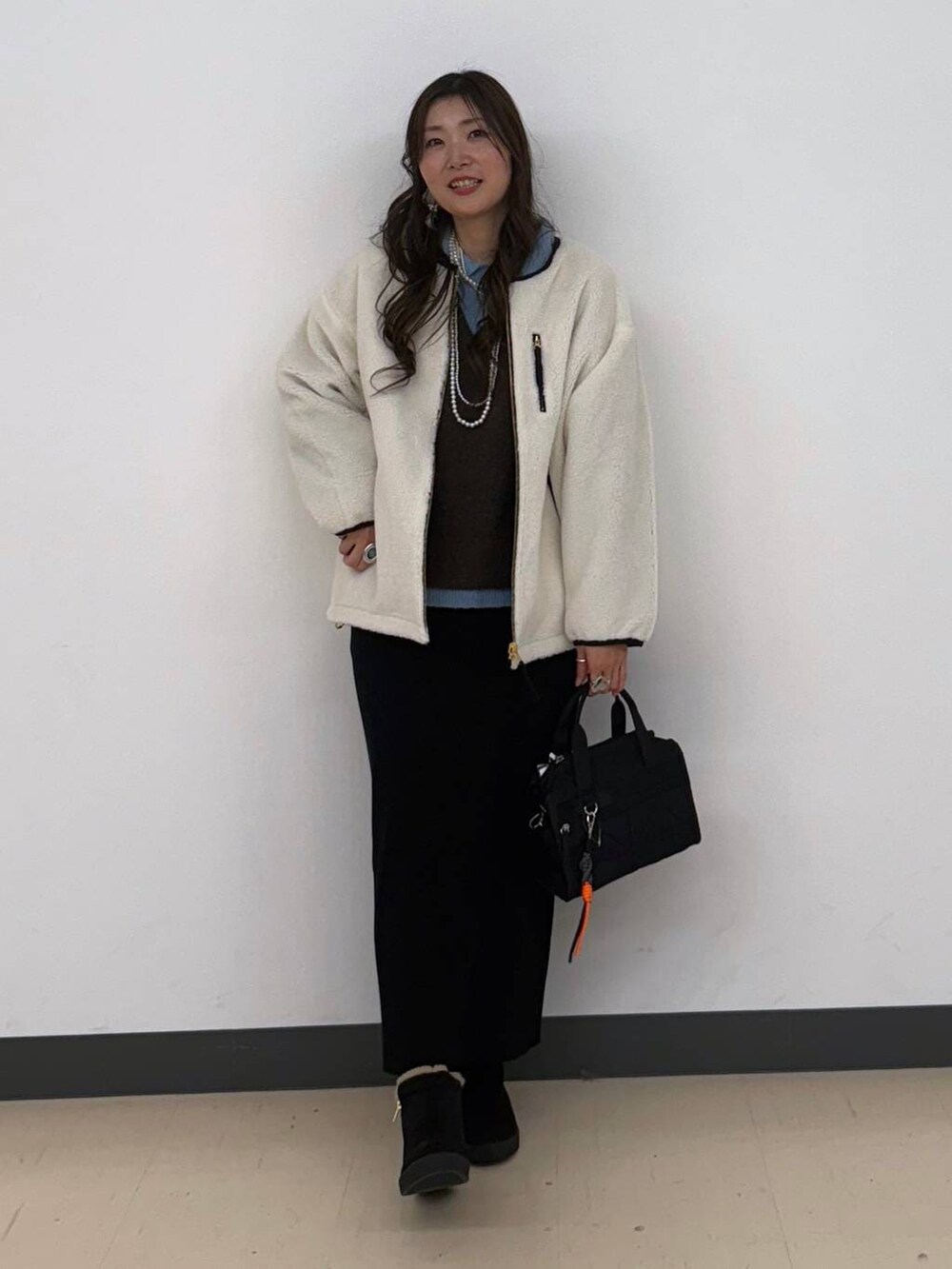 ホワイト系のブルゾン、ブラック系のボストンバッグ、ブラック系のスカートを着用したレディースの冬コーディネートの6枚目の写真