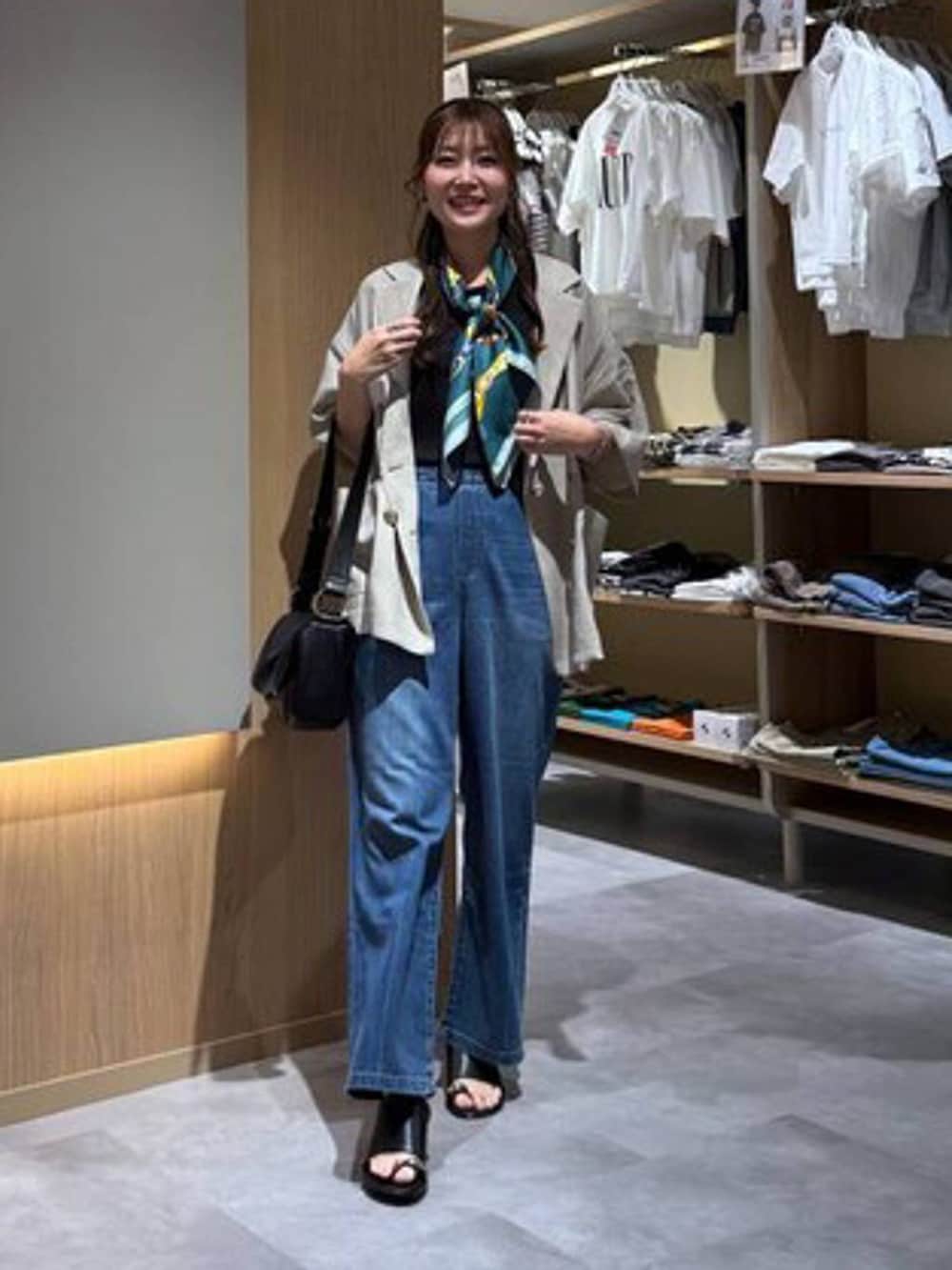 ブルー系のデニムパンツ、ベージュ系のテーラードジャケット、ブラック系のサンダルを着用したレディースの夏コーディネートの2枚目の写真