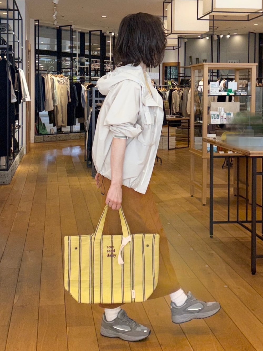 イエロー系のTシャツ/カットソー、ブラウン系のスカート、ホワイト系のナイロンジャケットを着用したレディースの春コーディネートの2枚目の写真