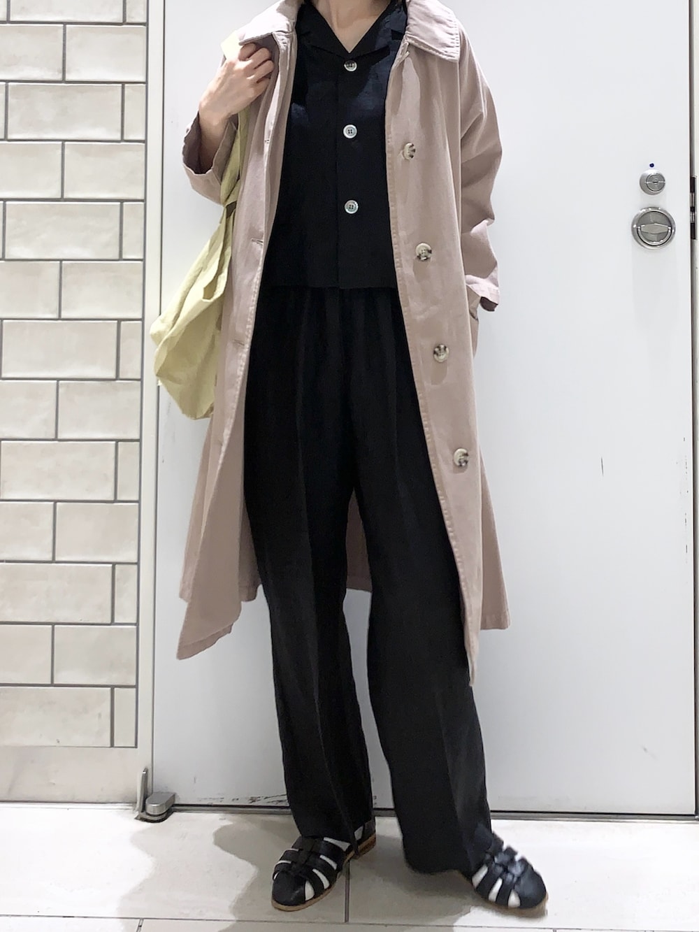 イエロー系のトートバッグ、ベージュ系のステンカラーコート、ブラック系のその他パンツを着用したレディースの春コーディネートの5枚目の写真
