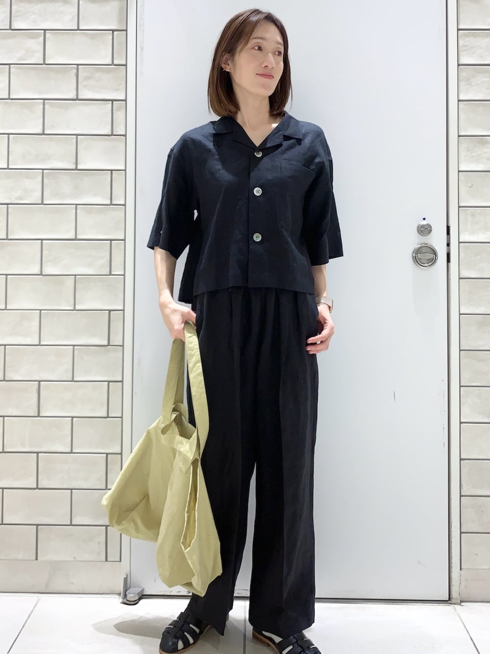 イエロー系のトートバッグ、ベージュ系のステンカラーコート、ブラック系のその他パンツを着用したレディースの春コーディネートの3枚目の写真