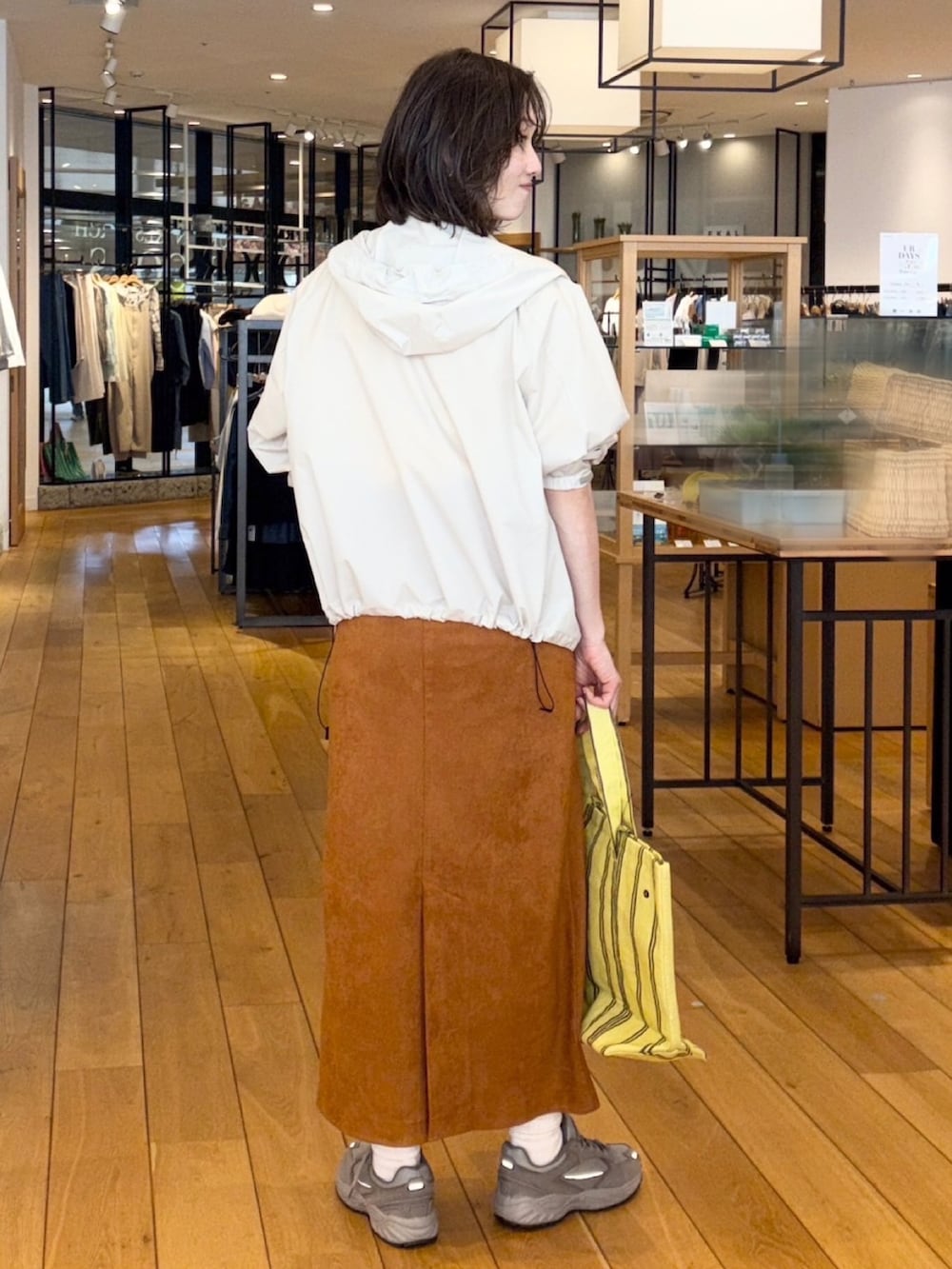 イエロー系のTシャツ/カットソー、ブラウン系のスカート、ホワイト系のナイロンジャケットを着用したレディースの春コーディネートの3枚目の写真