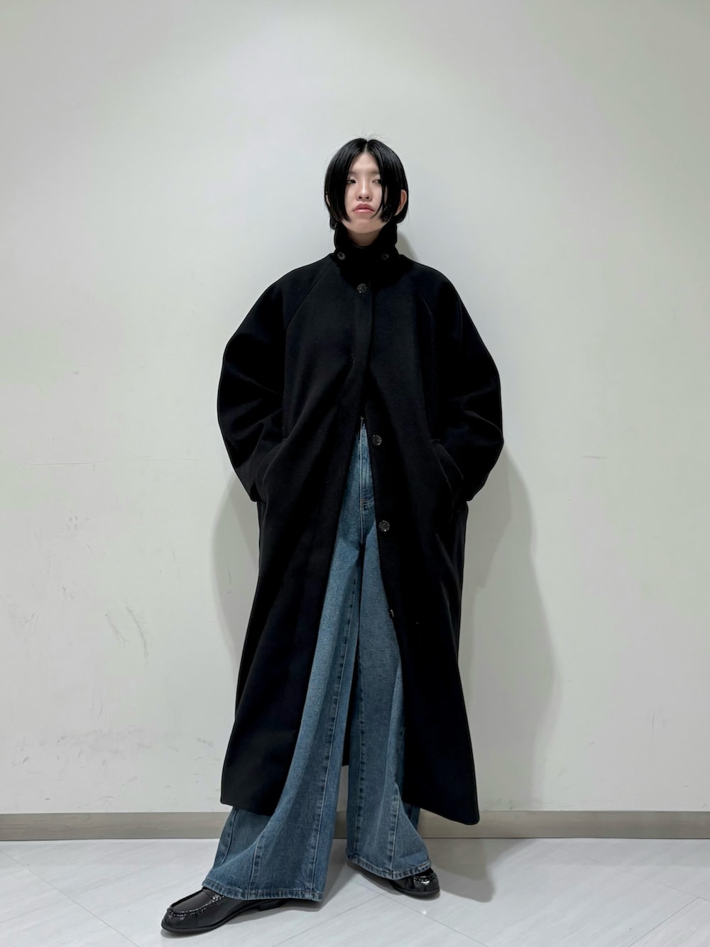 ブラック系のステンカラーコート、ブルー系のデニムパンツ、ブラック系のその他シューズを着用したレディースの秋コーディネートの2枚目の写真