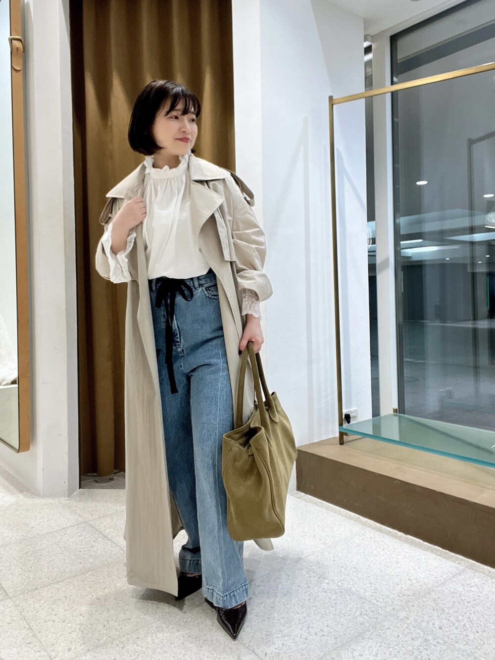 ベージュ系のトレンチコート、ブルー系のデニムパンツ、ホワイト系のシャツ/ブラウスを着用したレディースの秋コーディネートの2枚目の写真