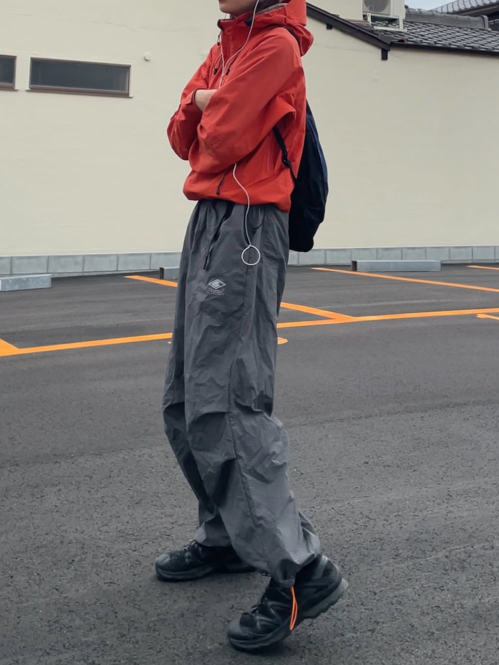 オレンジ系のマウンテンパーカー、グレー系のパンツ、ブラック系のスニーカーを着用したメンズの春コーディネートの2枚目の写真