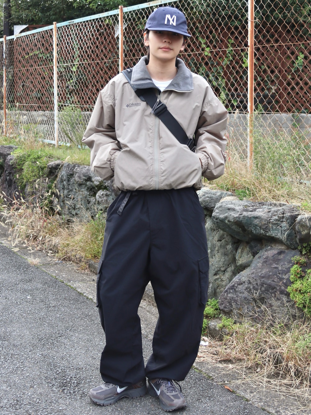 グレー系のショルダーバッグ、グレー系のスニーカー、ブラック系のカーゴパンツを着用したメンズの秋コーディネートの2枚目の写真