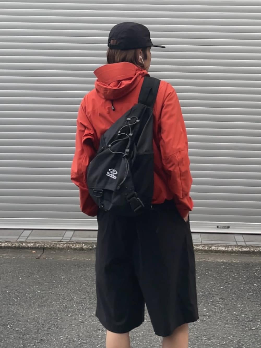 オレンジ系のマウンテンパーカー、ブラック系のショルダーバッグ、ブラック系のカーゴパンツを着用したメンズの夏コーディネートの3枚目の写真