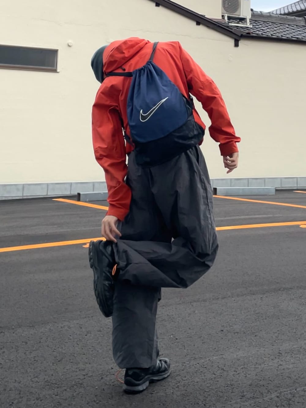 オレンジ系のマウンテンパーカー、グレー系のパンツ、ブラック系のスニーカーを着用したメンズの春コーディネートの3枚目の写真