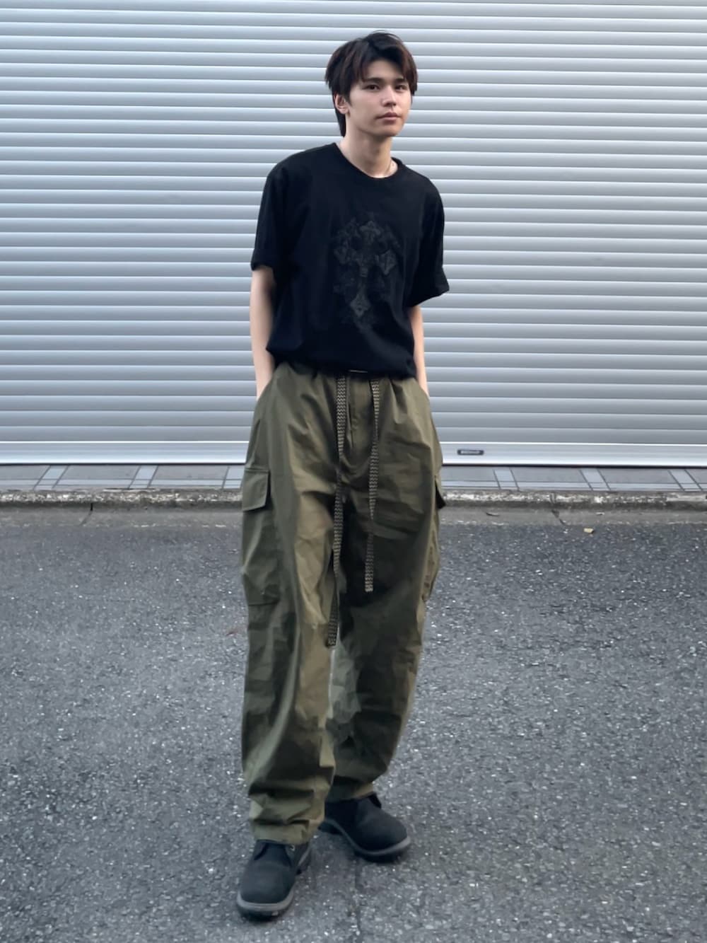 グリーン系のカーゴパンツ、ブラック系のTシャツ/カットソー、ブラック系のブーツを着用したメンズの夏コーディネートの2枚目の写真