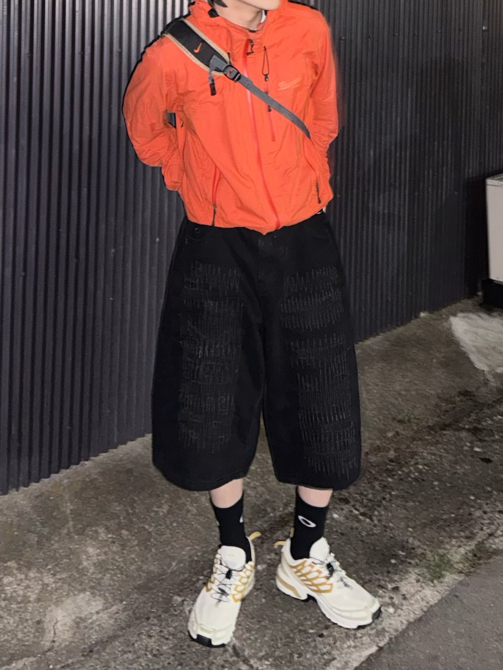 ホワイト系のスニーカー、オレンジ系のマウンテンパーカー、ブラック系のデニムパンツを着用したメンズの秋コーディネートの3枚目の写真