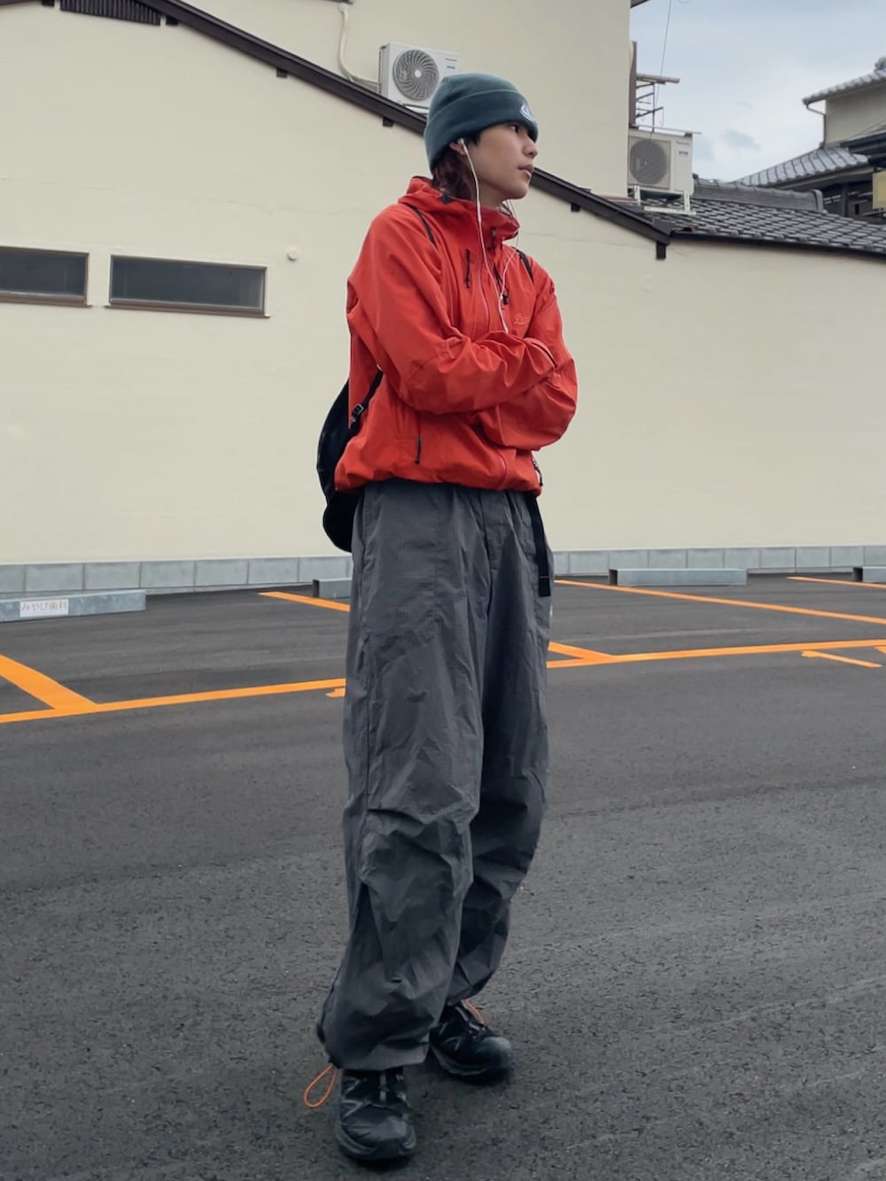 オレンジ系のマウンテンパーカー、グレー系のパンツ、ブラック系のスニーカーを着用したメンズの春コーディネートの4枚目の写真