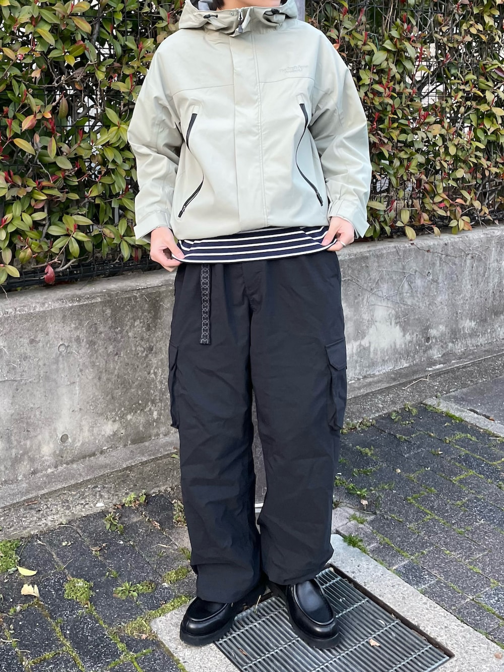 グリーン系のマウンテンパーカー、ホワイト系のTシャツ/カットソー、ブラック系のドレスシューズを着用したメンズの春コーディネートの2枚目の写真