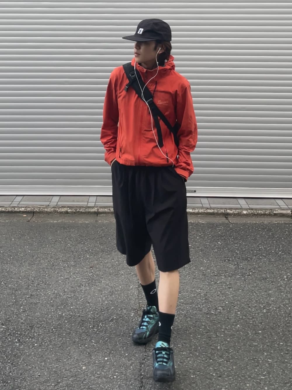 オレンジ系のマウンテンパーカー、ブラック系のショルダーバッグ、ブラック系のカーゴパンツを着用したメンズの夏コーディネートの2枚目の写真