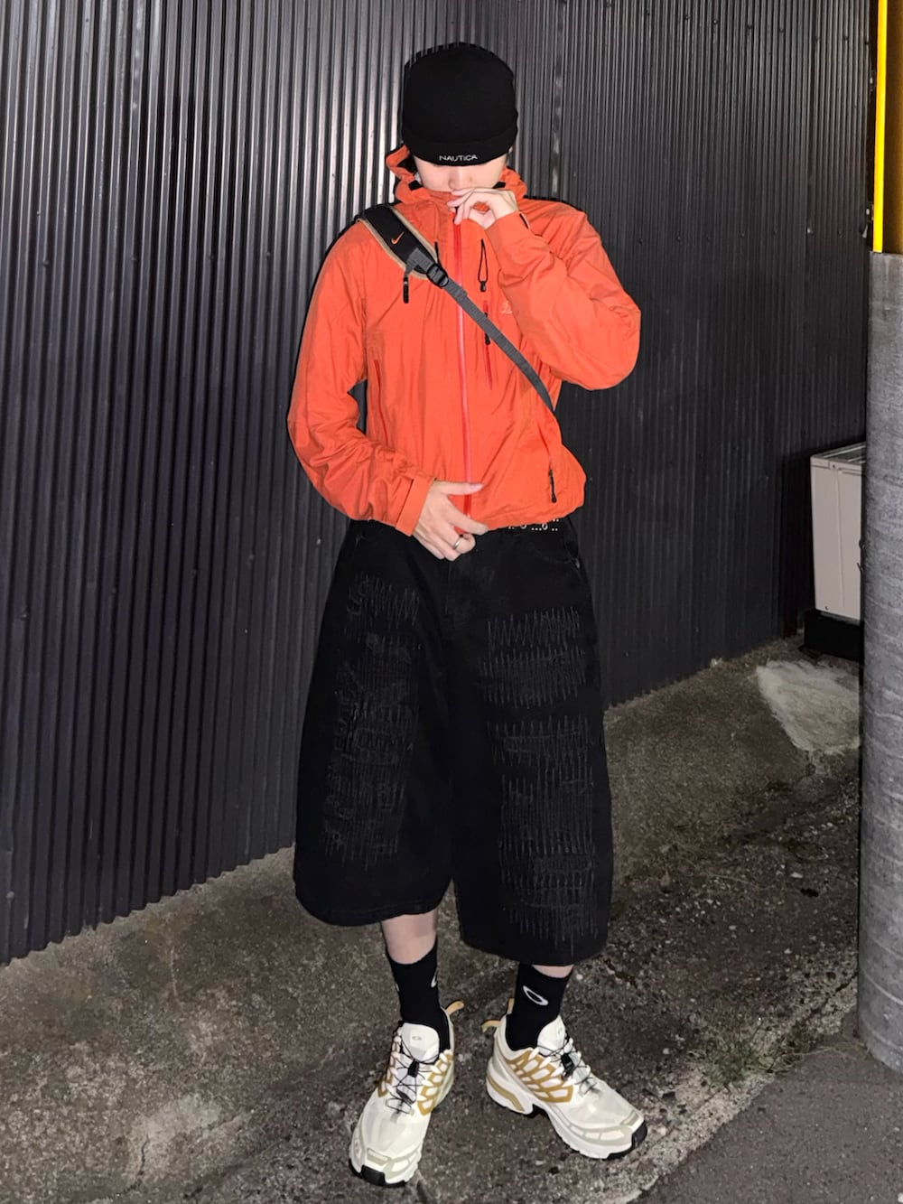 ホワイト系のスニーカー、オレンジ系のマウンテンパーカー、ブラック系のデニムパンツを着用したメンズの秋コーディネートの2枚目の写真