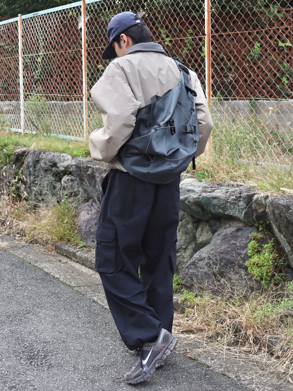 グレー系のショルダーバッグ、グレー系のスニーカー、ブラック系のカーゴパンツを着用したメンズの秋コーディネートの3枚目の写真