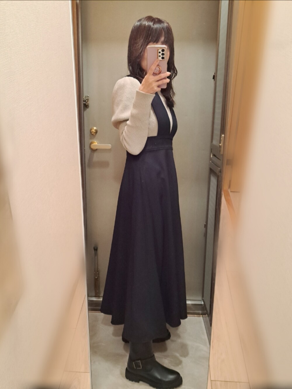 ブラック系のジャンパースカート、ベージュ系のニット/セーター、ブラック系のブーツを着用したレディースの冬コーディネートの2枚目の写真