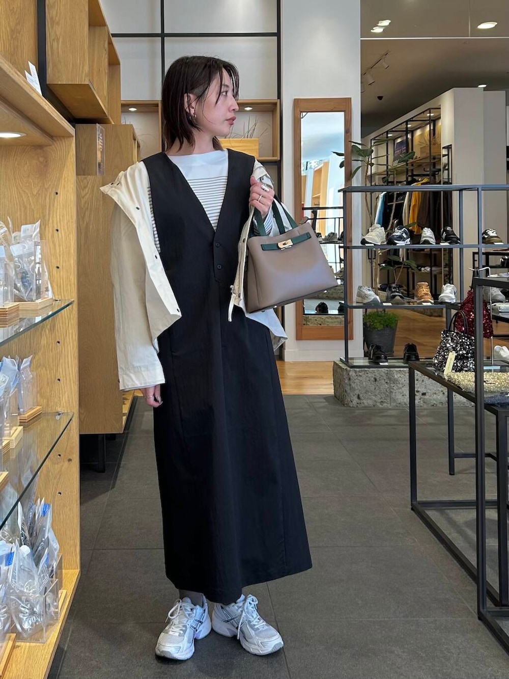 ホワイト系のスニーカー、ブラック系のジャンパースカート、ベージュ系のハンドバッグを着用したレディースの冬コーディネートの2枚目の写真