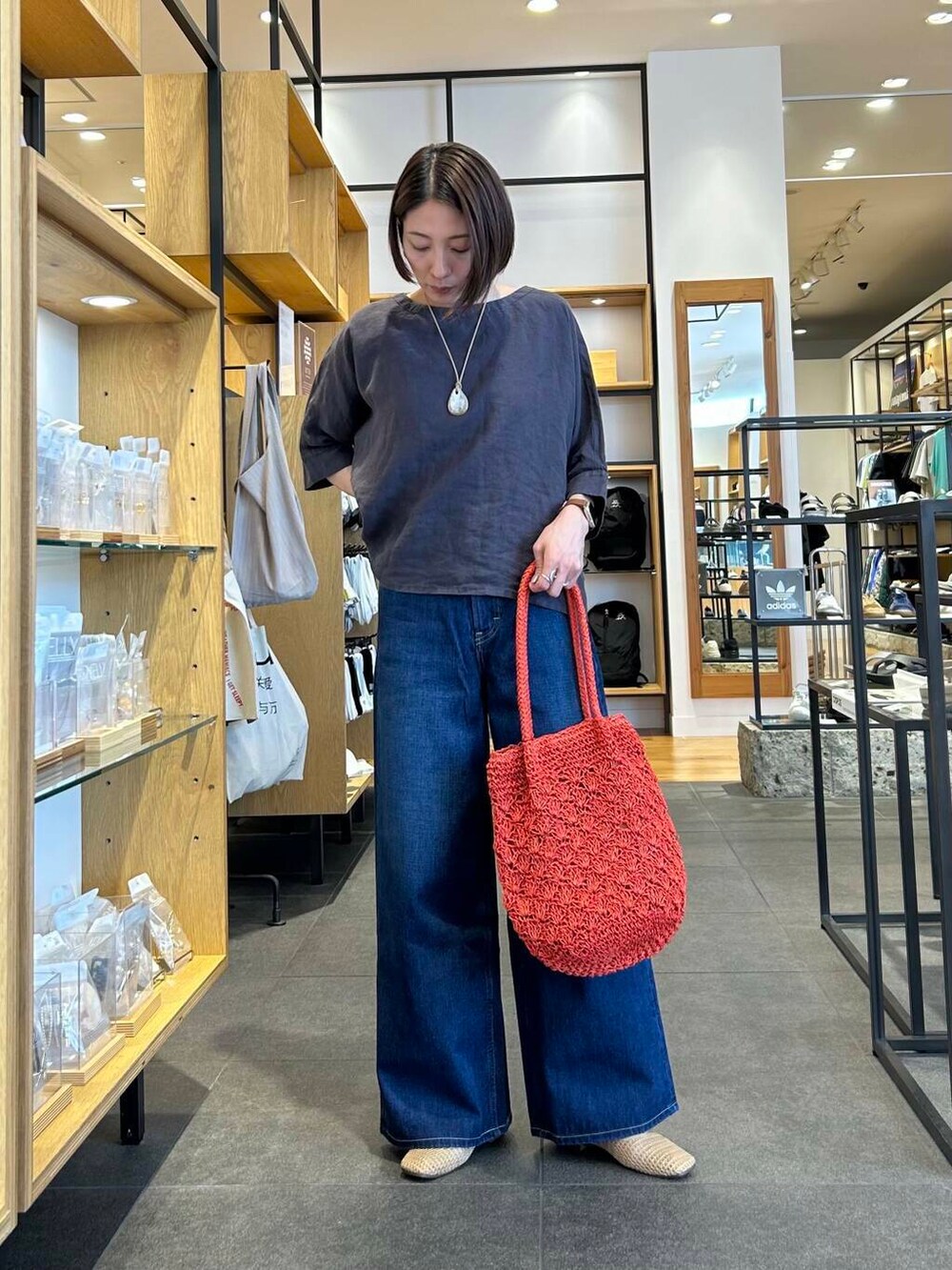 ブルー系のデニムパンツ、オレンジ系のトートバッグ、ベージュ系のバレエシューズを着用したレディースの夏コーディネートの2枚目の写真