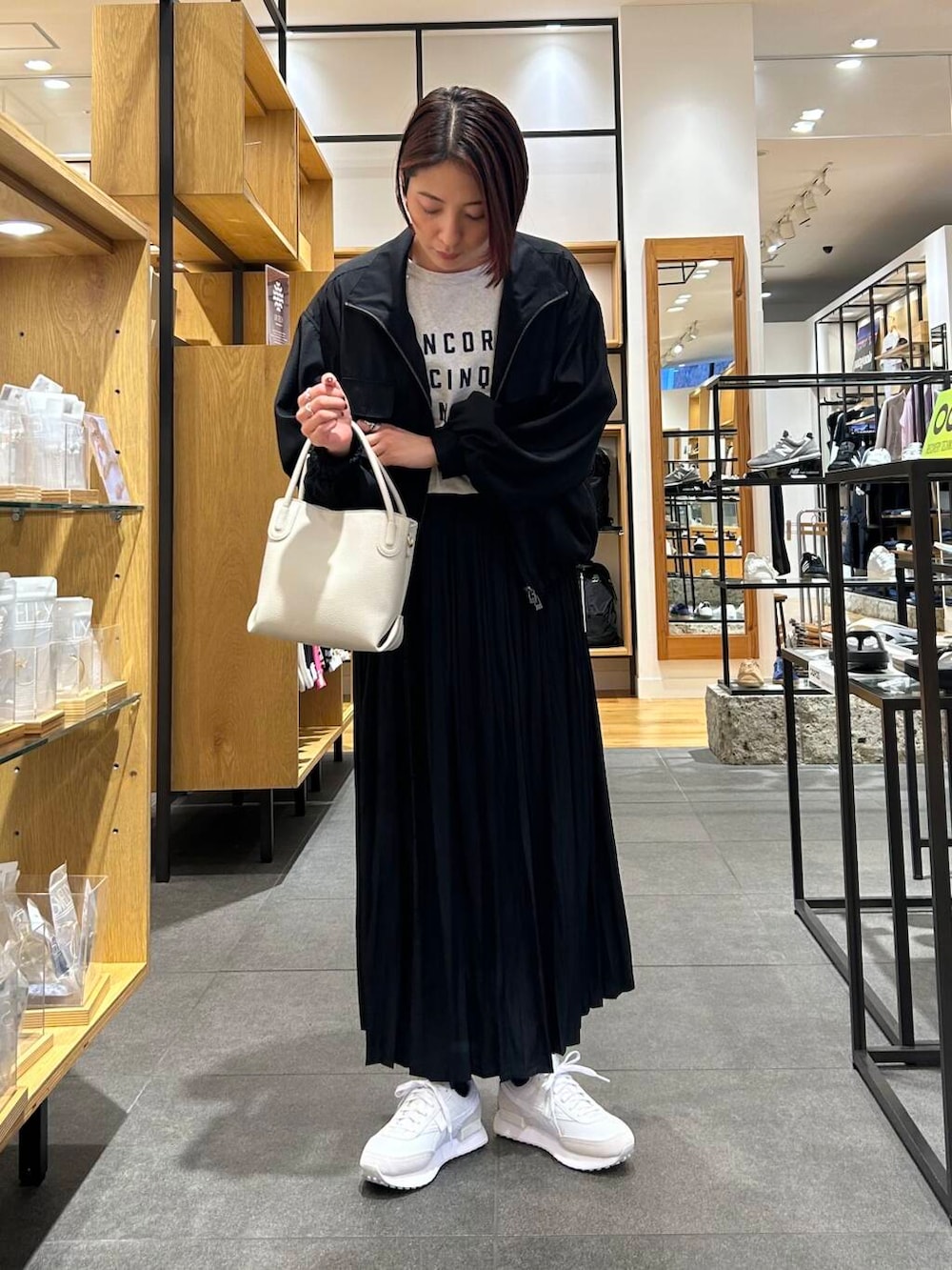 ホワイト系のハンドバッグ、ホワイト系のスニーカー、ブラック系のブルゾンを着用したレディースの春コーディネートの4枚目の写真