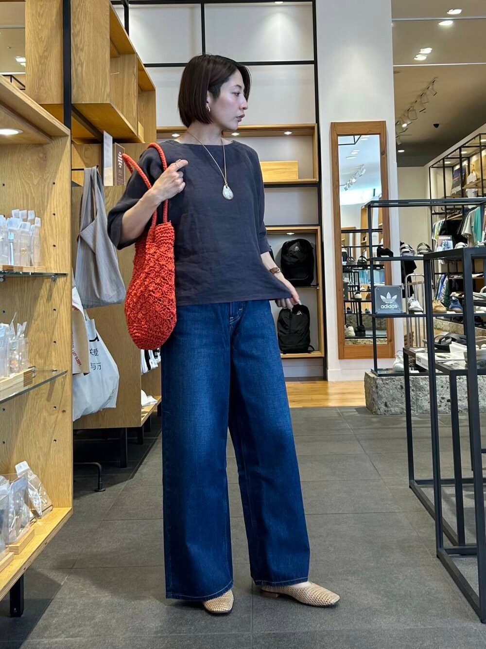 ブルー系のデニムパンツ、オレンジ系のトートバッグ、ベージュ系のバレエシューズを着用したレディースの夏コーディネートの3枚目の写真