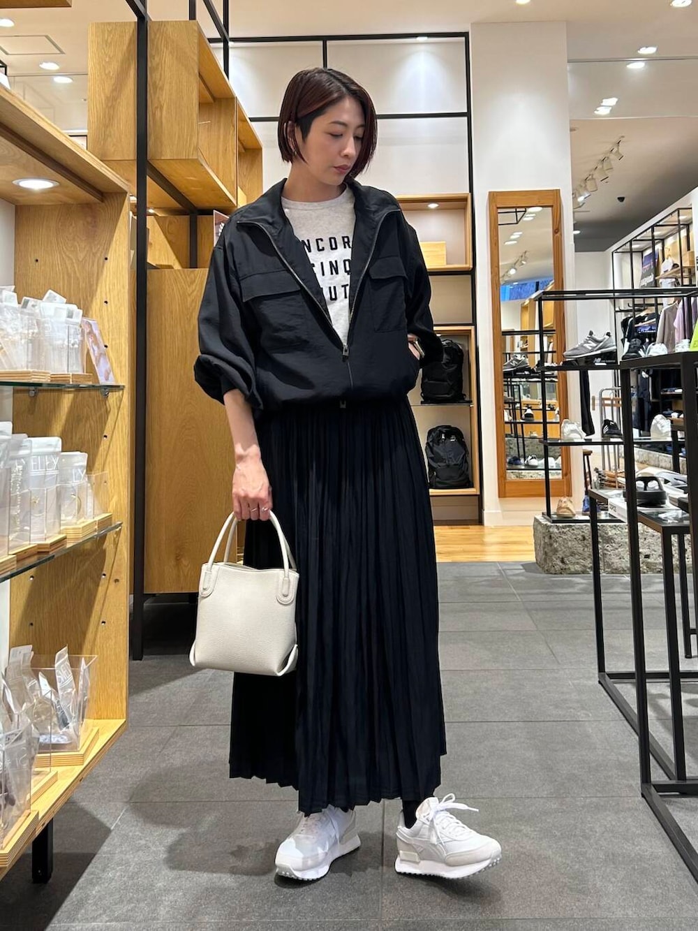 ホワイト系のハンドバッグ、ホワイト系のスニーカー、ブラック系のブルゾンを着用したレディースの春コーディネートの2枚目の写真