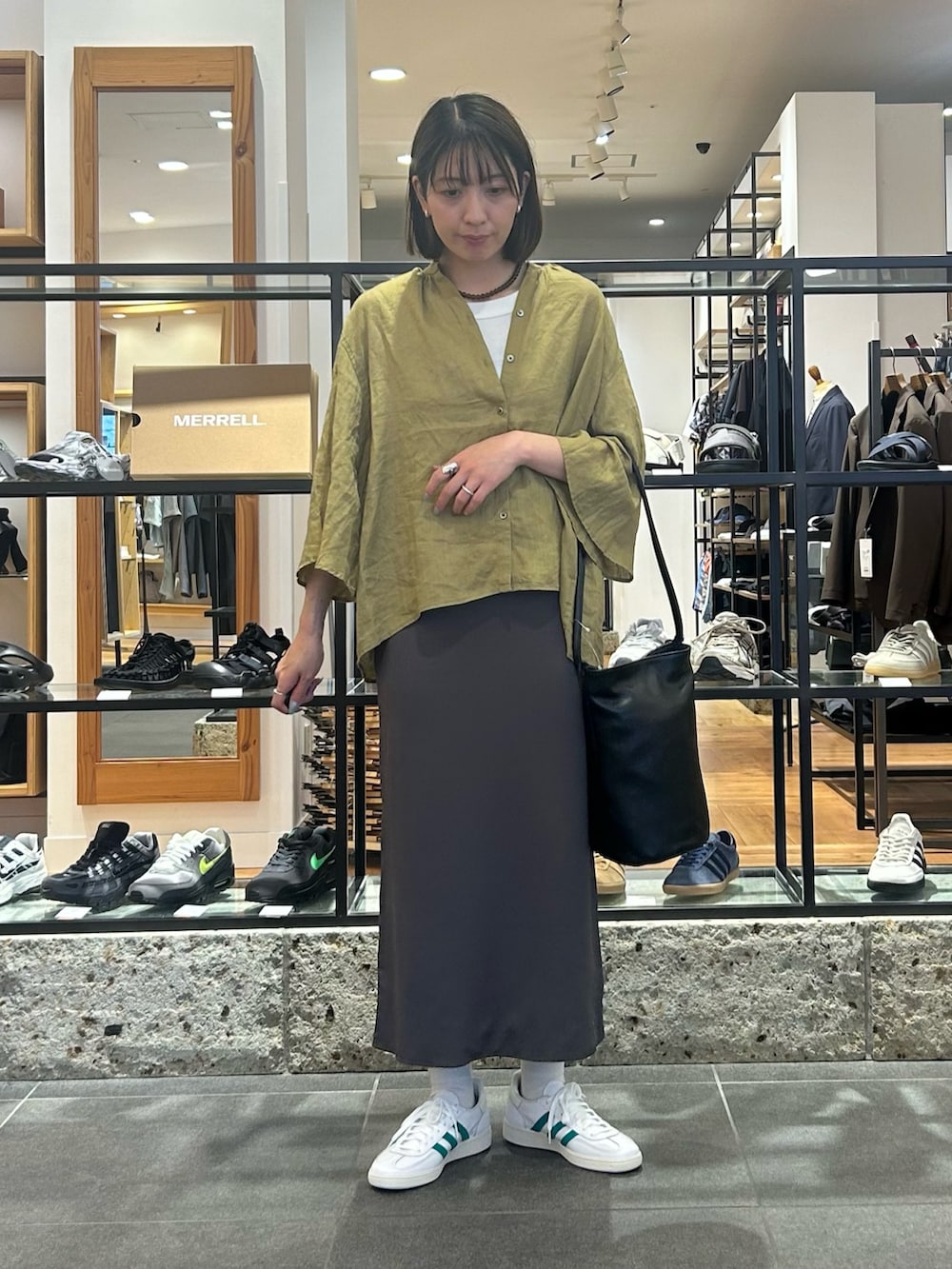グレー系のスカート、ホワイト系のスニーカー、ブラック系のショルダーバッグを着用したレディースの春コーディネートの2枚目の写真
