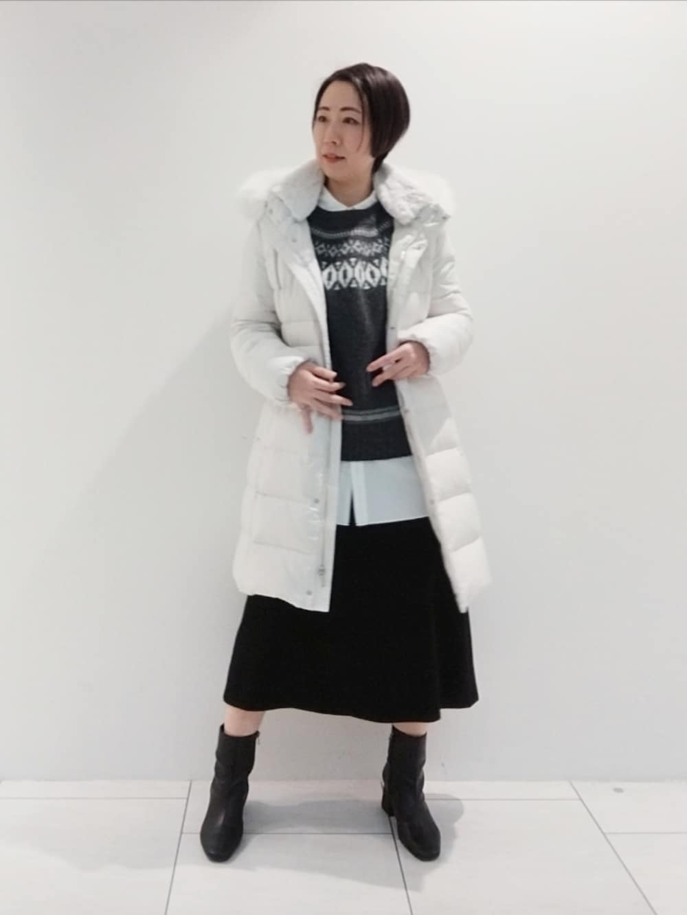 グレー系のニット/セーター、ホワイト系のシャツ/ブラウス、グレー系のダウンジャケット/コートを着用したレディースの冬コーディネートの2枚目の写真