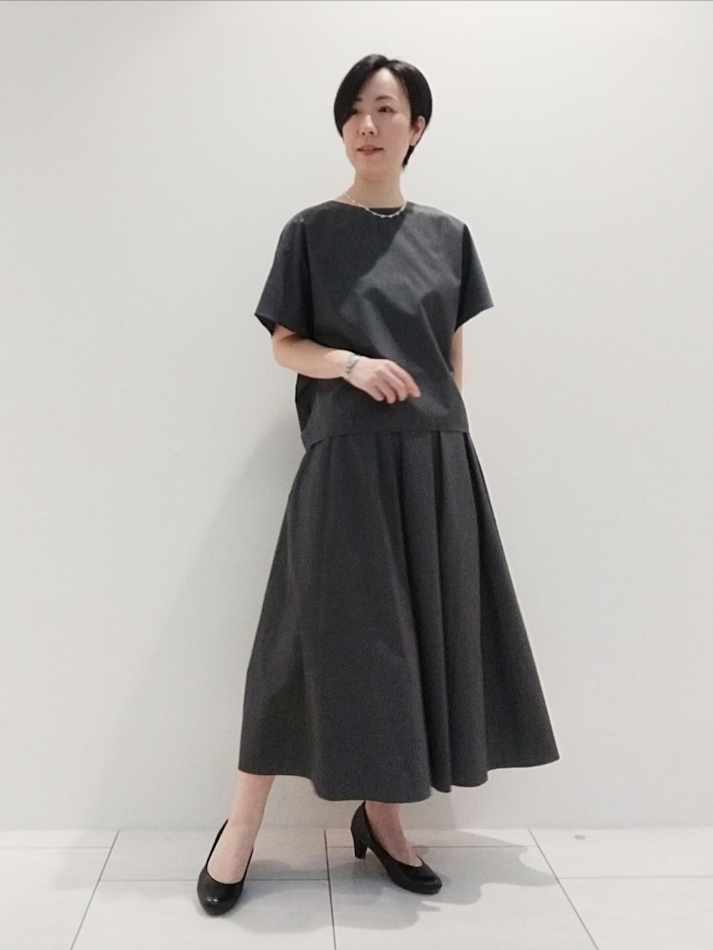 グレー系のシャツ/ブラウス、グレー系のスカート、シルバー系のネックレスを着用したレディースの夏コーディネートの2枚目の写真