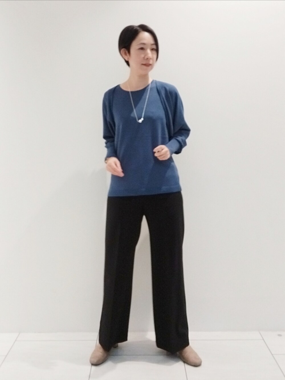 ブルー系のアンサンブル、ブラック系のスーツパンツ、シルバー系のネックレスを着用したレディースの秋コーディネートの2枚目の写真