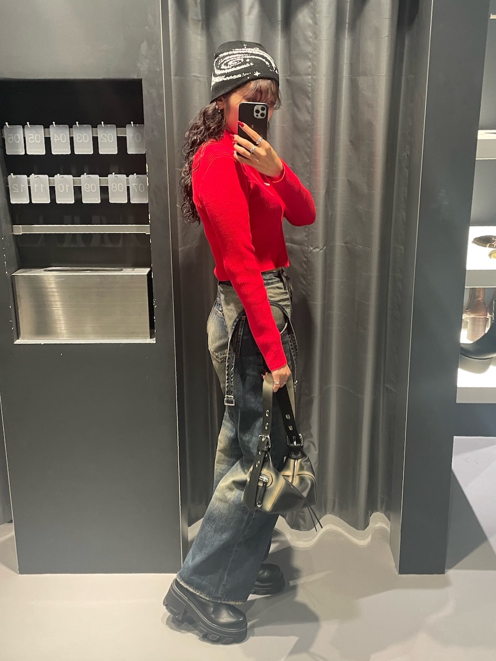 レッド系のニット/セーター、ブルー系のデニムパンツ、ブラック系のハンドバッグを着用したレディースの秋コーディネートの2枚目の写真