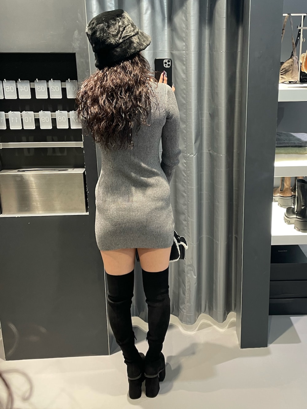 グレー系のワンピース、ブラック系のハンドバッグ、ブラック系のブーツを着用したレディースの冬コーディネートの3枚目の写真