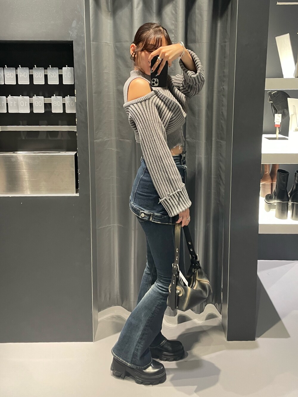 グレー系のニット/セーター、ブルー系のデニムパンツ、ブラック系のハンドバッグを着用したレディースの秋コーディネートの2枚目の写真