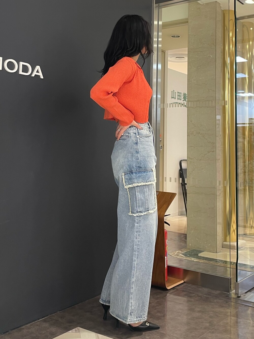 オレンジ系のニット/セーター、ブルー系のデニムパンツ、ブラック系のパンプスを着用したレディースの春コーディネートの2枚目の写真