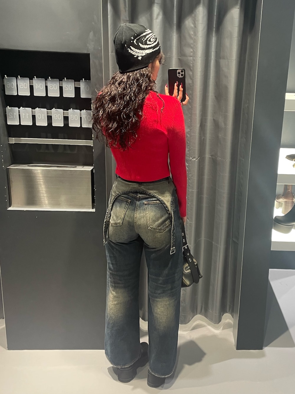 レッド系のニット/セーター、ブルー系のデニムパンツ、ブラック系のハンドバッグを着用したレディースの秋コーディネートの3枚目の写真