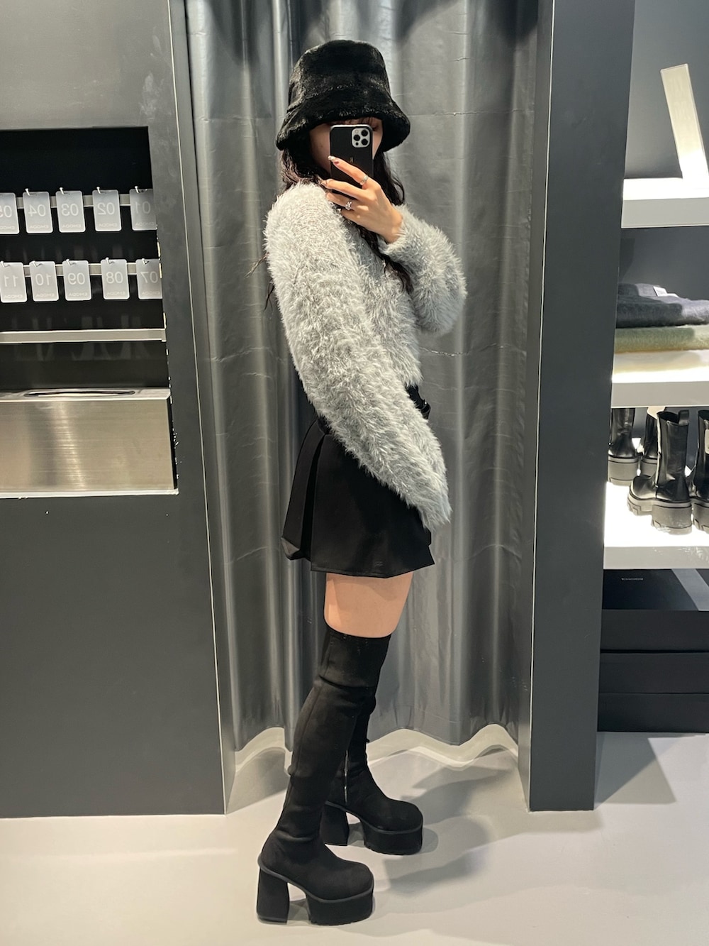 グレー系のニット/セーター、ブラック系のスカート、ブラック系のブーツを着用したレディースの秋コーディネートの2枚目の写真