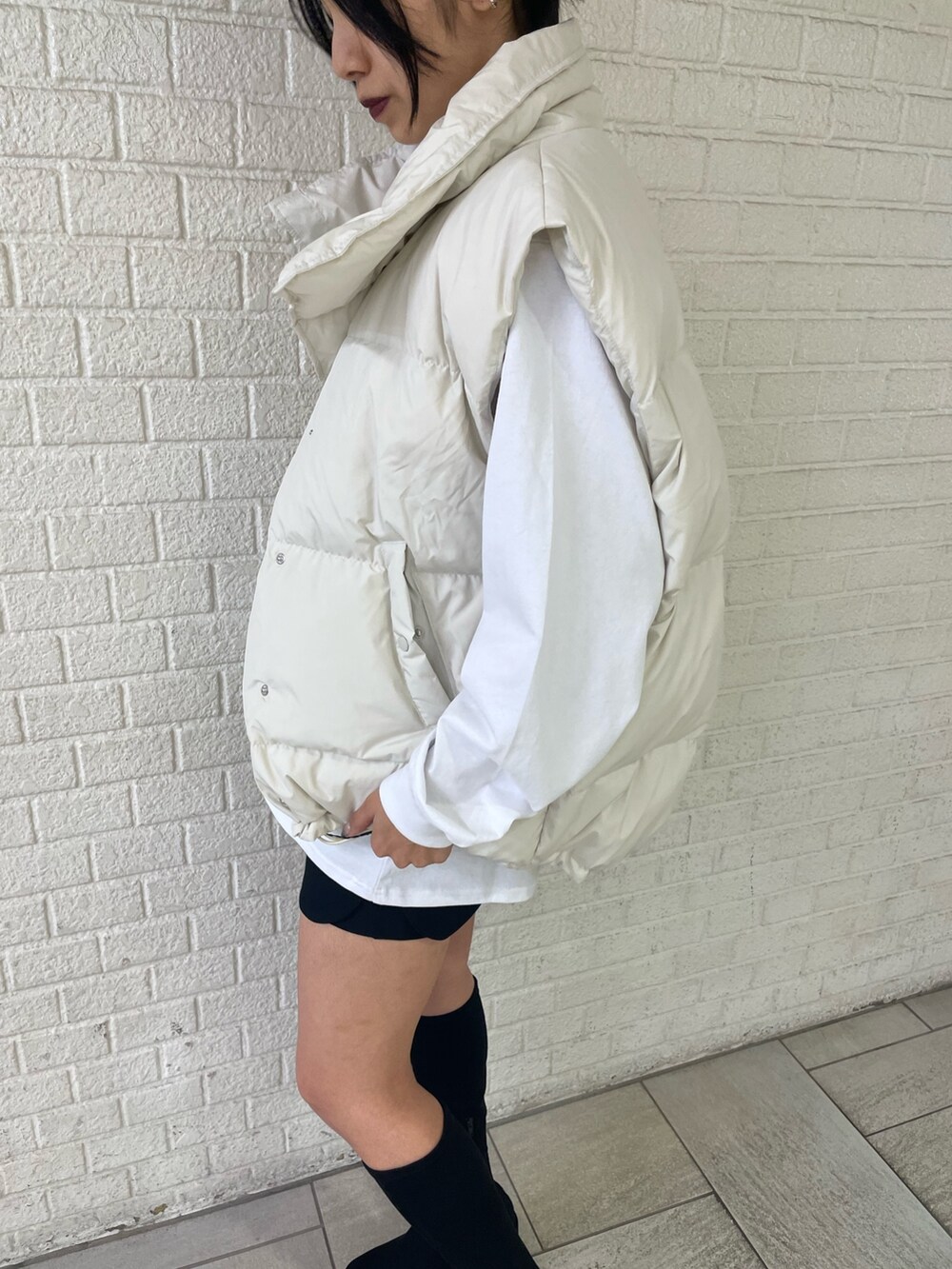 ホワイト系のTシャツ/カットソー、ホワイト系のダウンベスト、ブラック系のスカートを着用したレディースの秋コーディネートの6枚目の写真