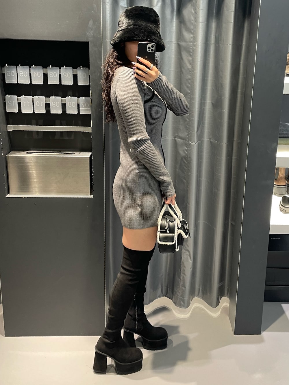 グレー系のワンピース、ブラック系のハンドバッグ、ブラック系のブーツを着用したレディースの冬コーディネートの2枚目の写真