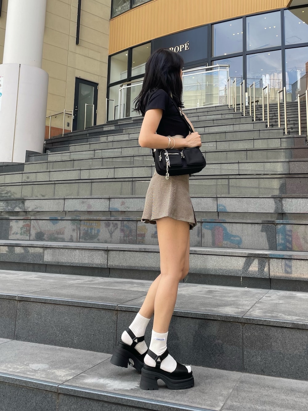 ブラック系のサンダル、ブラック系のTシャツ/カットソー、ブラック系のハンドバッグを着用したレディースの夏コーディネートの2枚目の写真