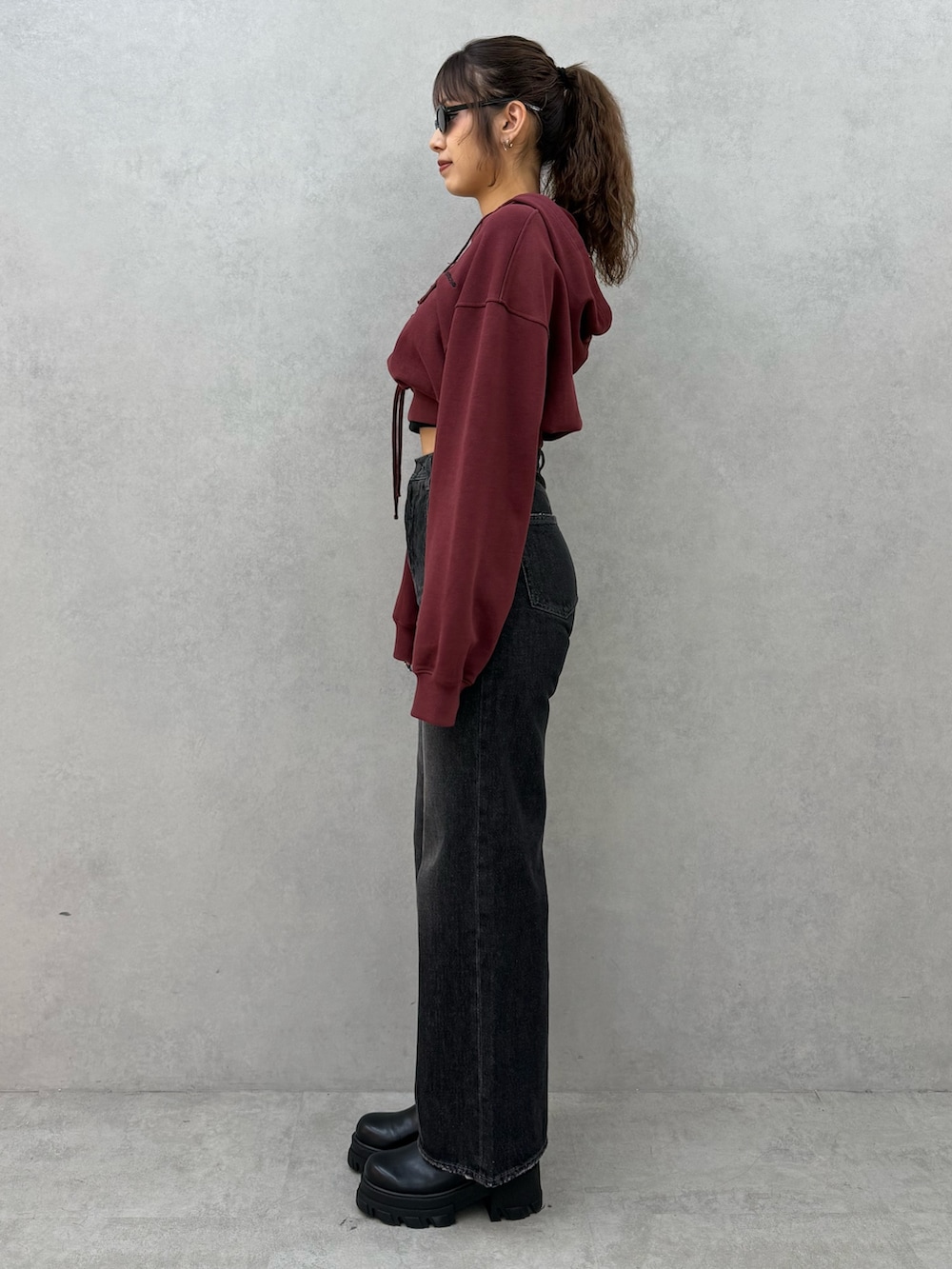 レッド系のパーカー、ブラック系のデニムパンツ、ブラック系のブーツを着用したレディースの秋コーディネートの2枚目の写真