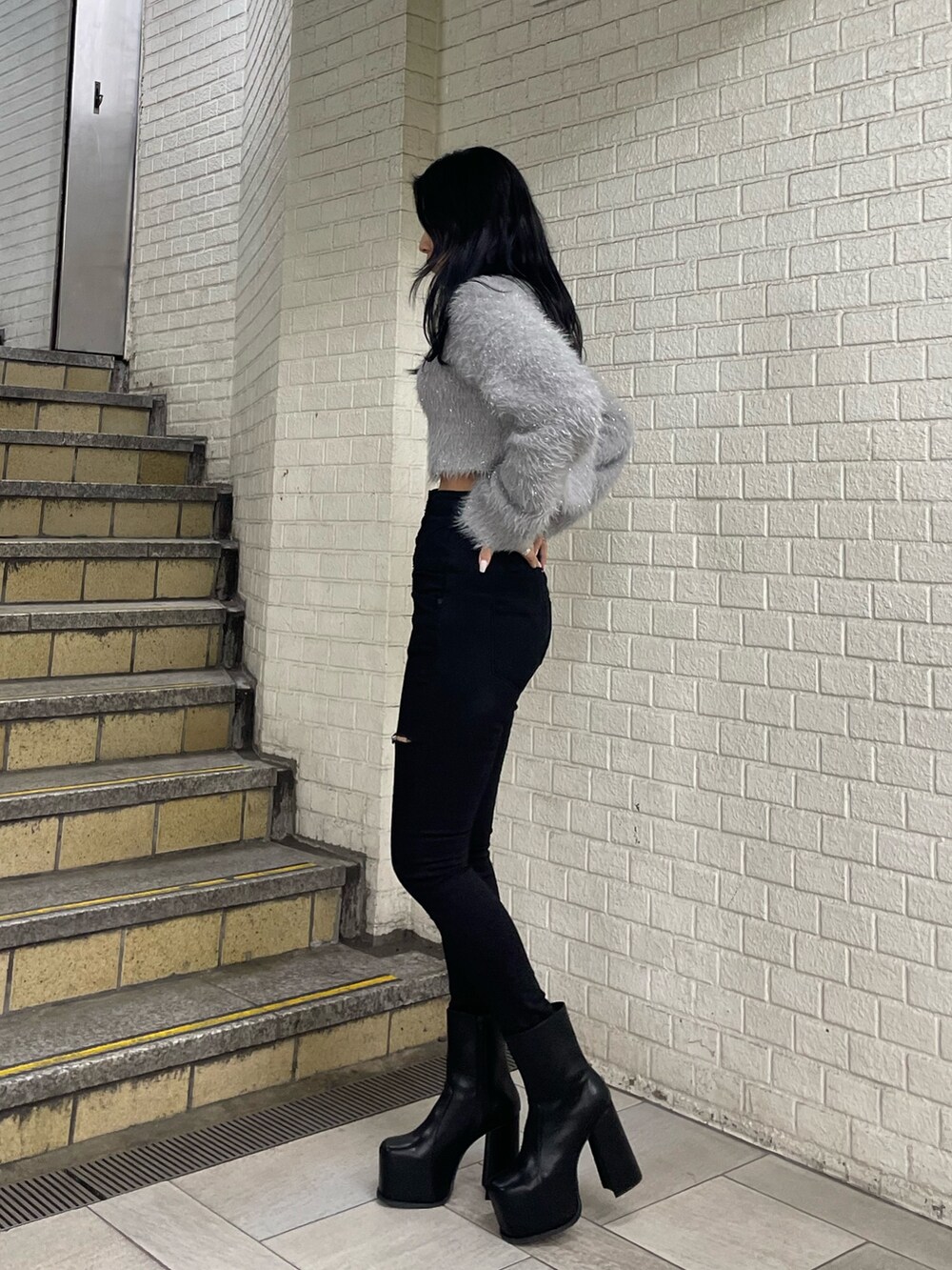 グレー系のニット/セーター、ブラック系のデニムパンツ、ブラック系のブーツを着用したレディースの冬コーディネートの2枚目の写真