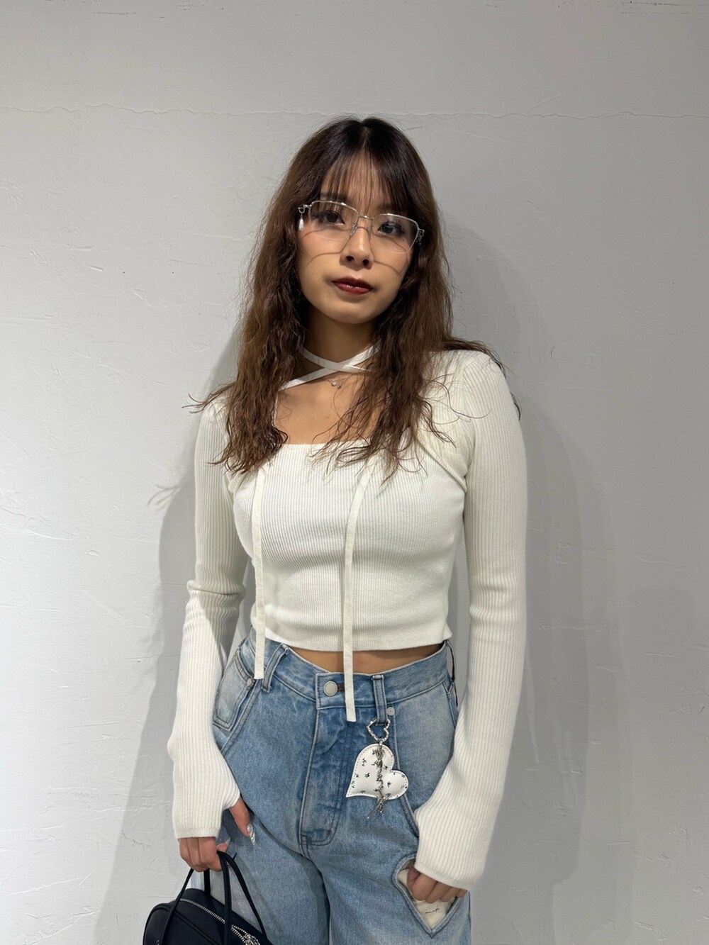 ホワイト系のニット/セーター、ブルー系のデニムパンツ、ブラック系のハンドバッグを着用したレディースの秋コーディネートの4枚目の写真