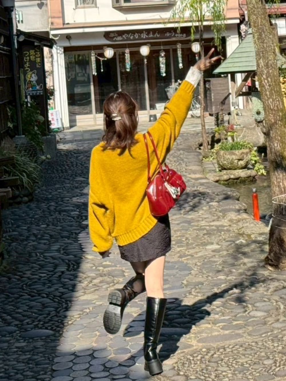 イエロー系のニット/セーター、レッド系のショルダーバッグ、ブラック系のブーツを着用したレディースの秋コーディネートの3枚目の写真