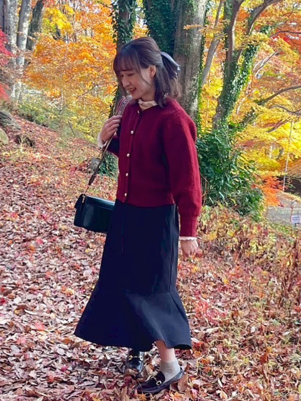 レッド系のカーディガン/ボレロ、ブラック系のショルダーバッグ、ブラウン系のローファーを着用したレディースの冬コーディネートの2枚目の写真