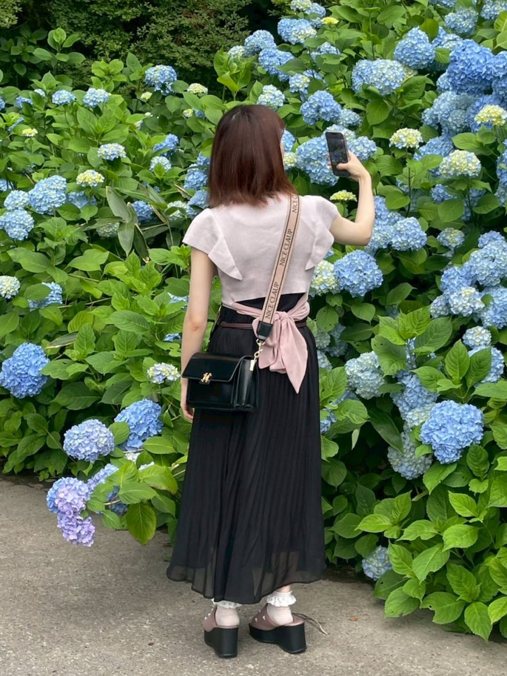 ピンク系のニット/セーター、ブラック系のショルダーバッグ、ブラック系のスカートを着用したレディースの夏コーディネートの2枚目の写真