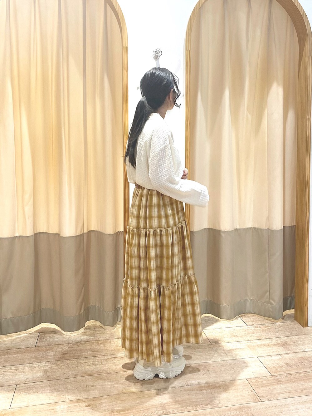 イエロー系のスカート、ホワイト系のカーディガン/ボレロ、ホワイト系のスニーカーを着用したレディースの春コーディネートの2枚目の写真